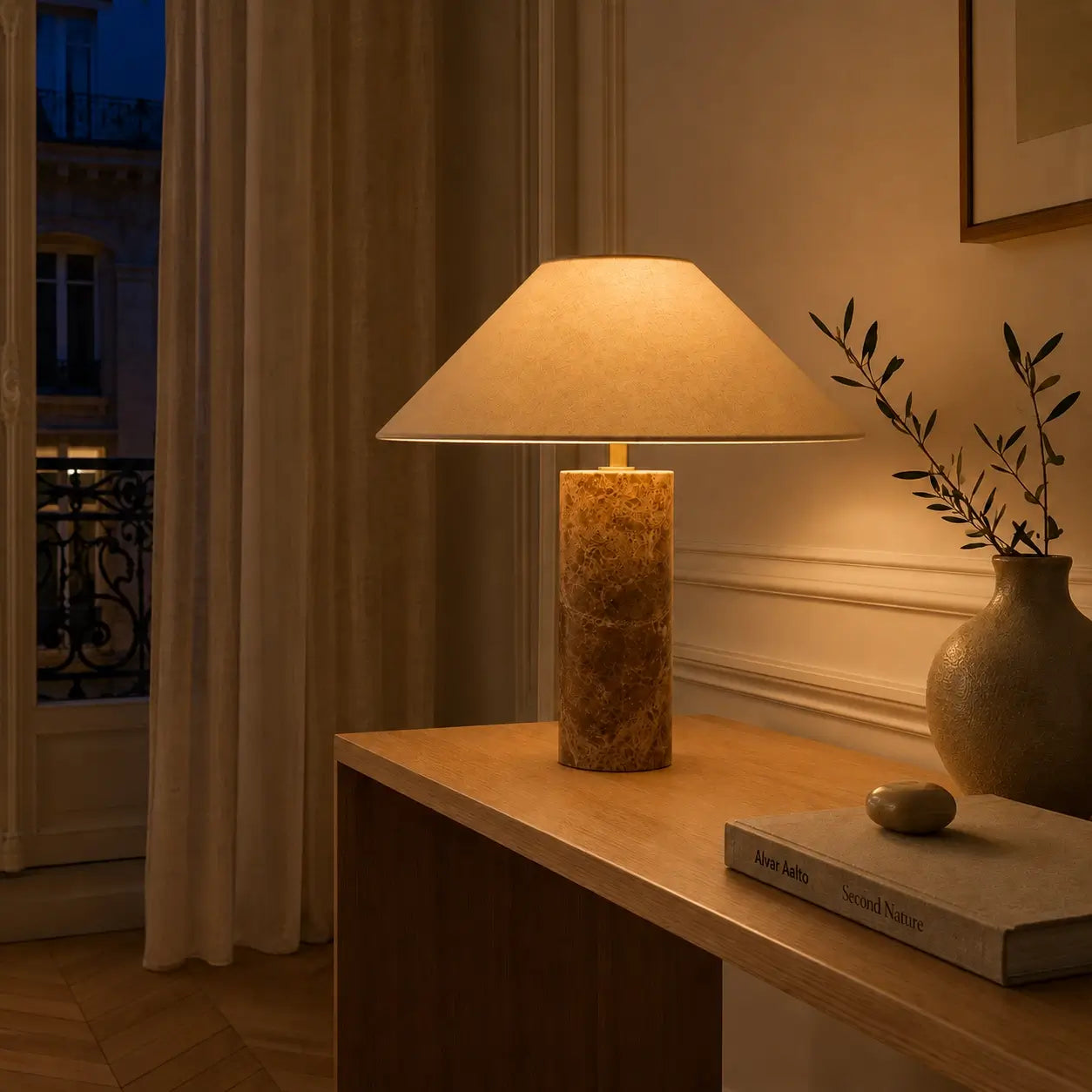 Lampe à poser Ara allumée le soir sur une console, diffusant une lumière chaude dans un salon parisien
