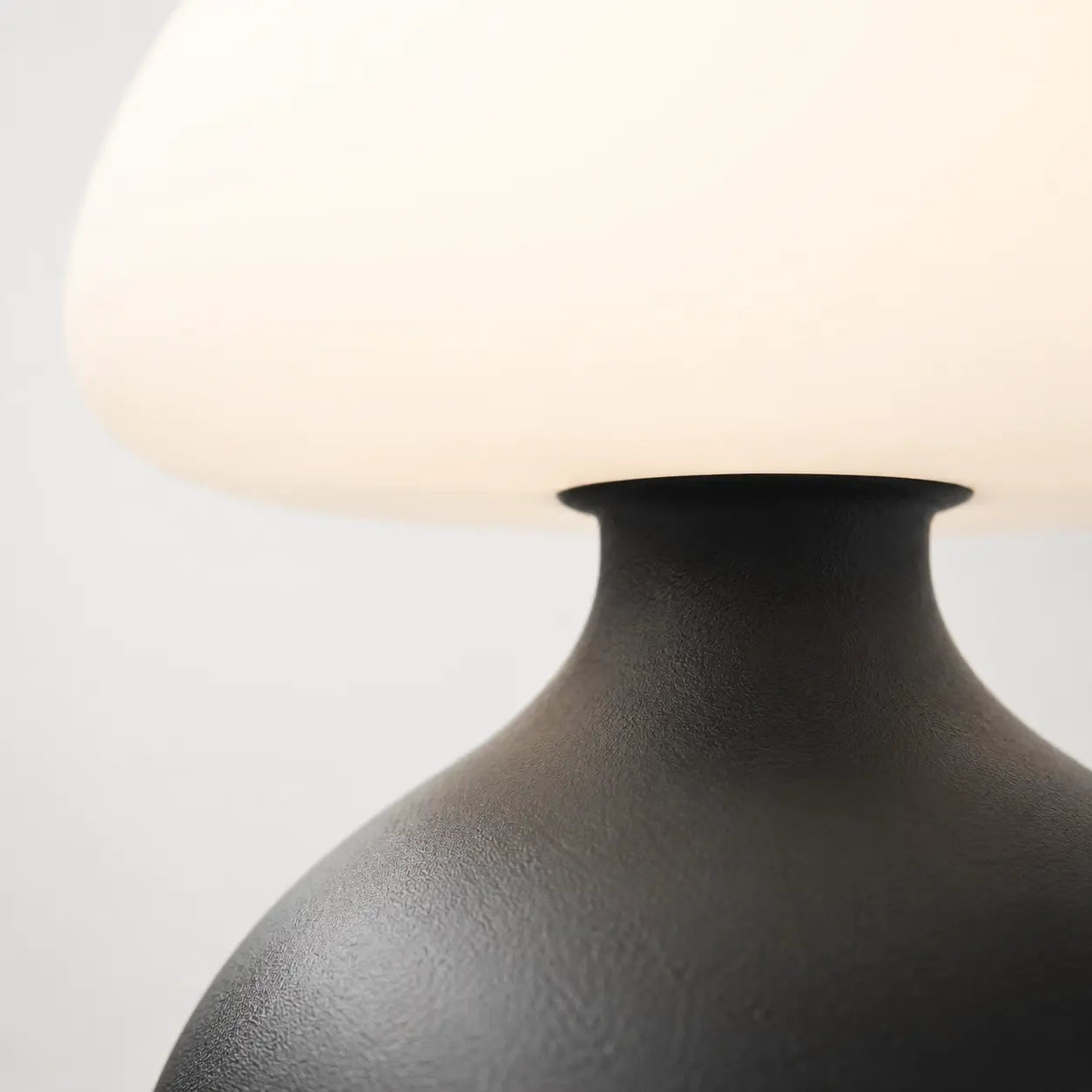 Détail de la lampe champignon Bulla : jonction entre le dôme en verre opale et la base en métal noir mat texturé