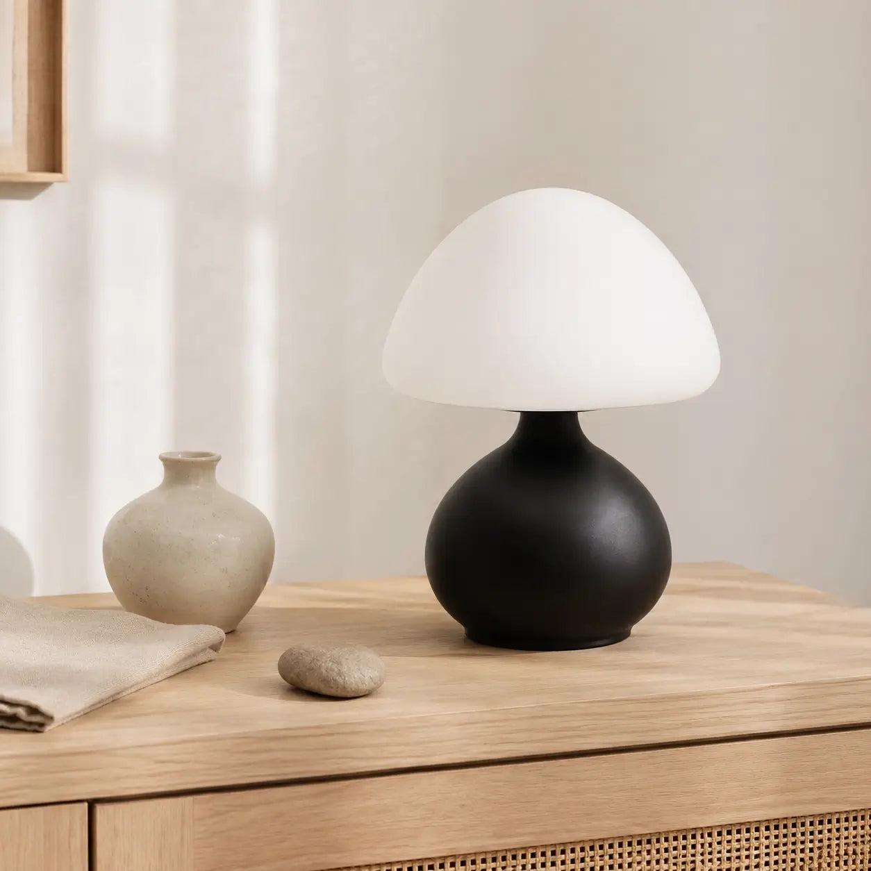 Lampe champignon Bulla noire à dôme opale posée sur un buffet en chêne parmi des objets minéraux aux tons naturels