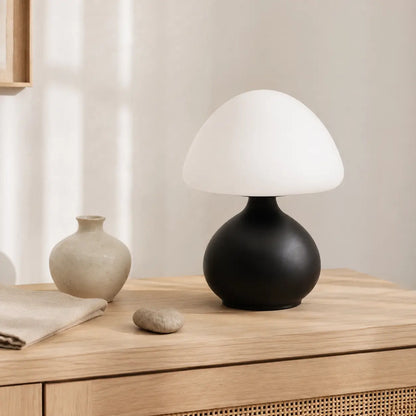 Lampe champignon Bulla noire à dôme opale posée sur un buffet en chêne parmi des objets minéraux aux tons naturels