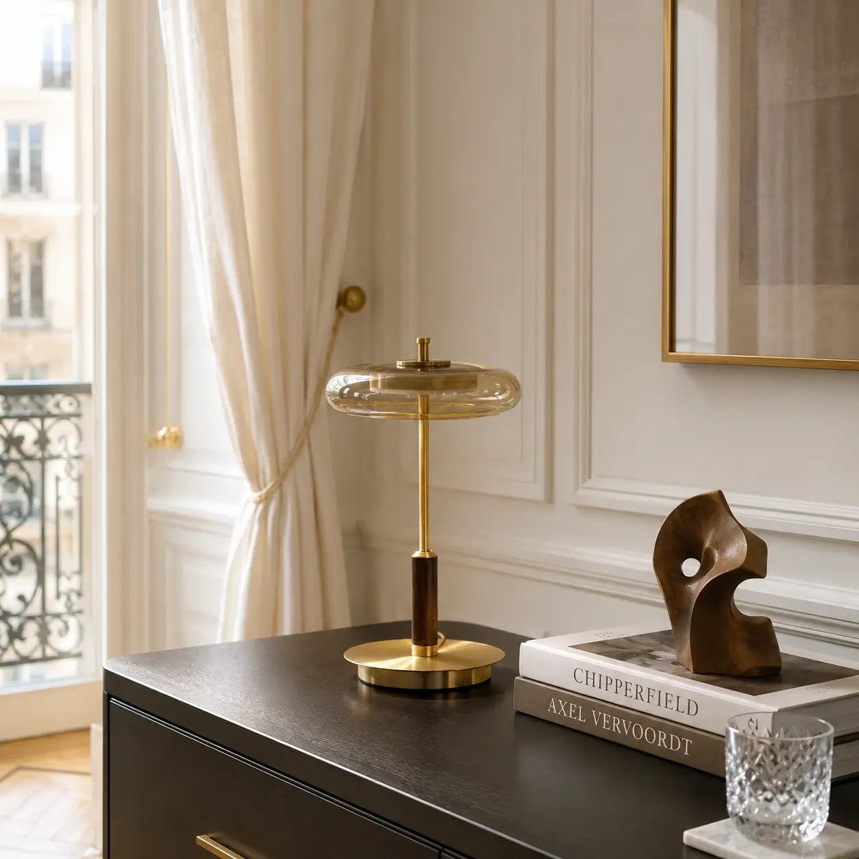 Lampe à poser Lentis en verre fumé et laiton posée sur une commode noire dans un intérieur haussmannien