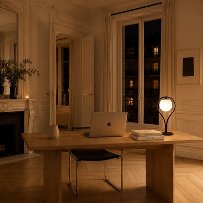 Lampe de bureau Halos allumée sur un grand bureau en chêne dans un bureau haussmannien parisien en soirée