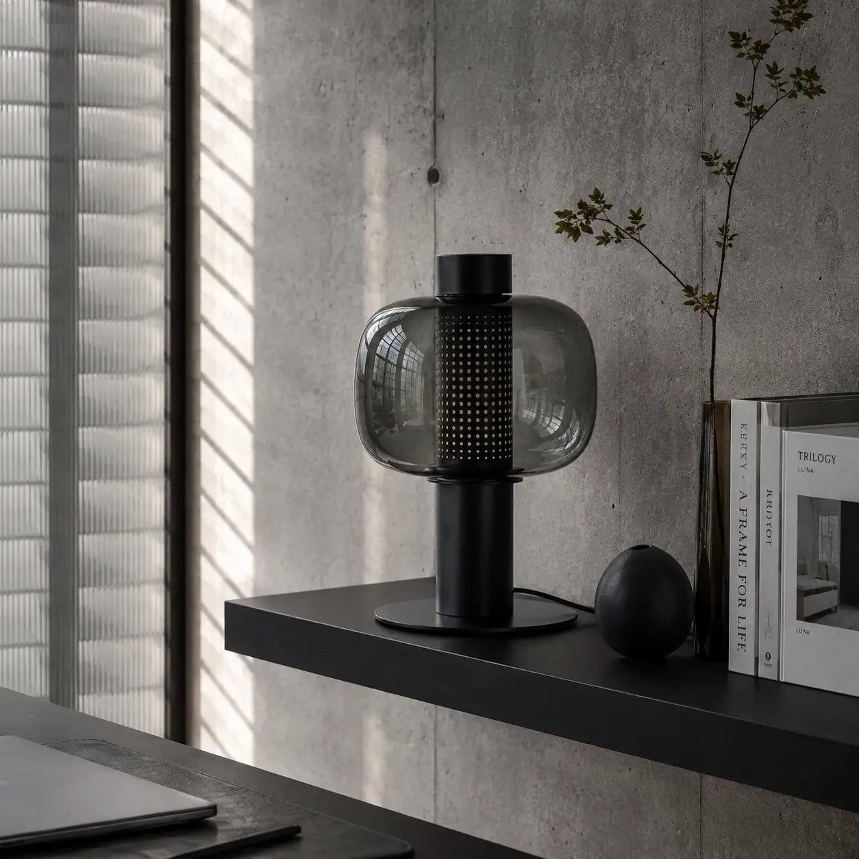 Lampe de bureau Astrum posée dans un intérieur béton brut avec jeux de lumière naturelle