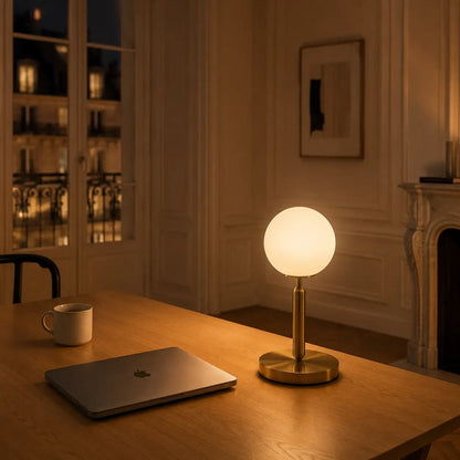 Lampe de bureau Luna à globe opale allumée sur un bureau en bois, lueur douce en soirée parisienne