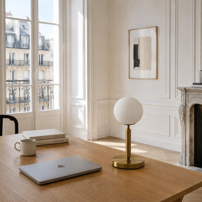 Lampe de bureau Luna à globe opale posée sur un bureau en chêne dans un intérieur haussmannien lumineux