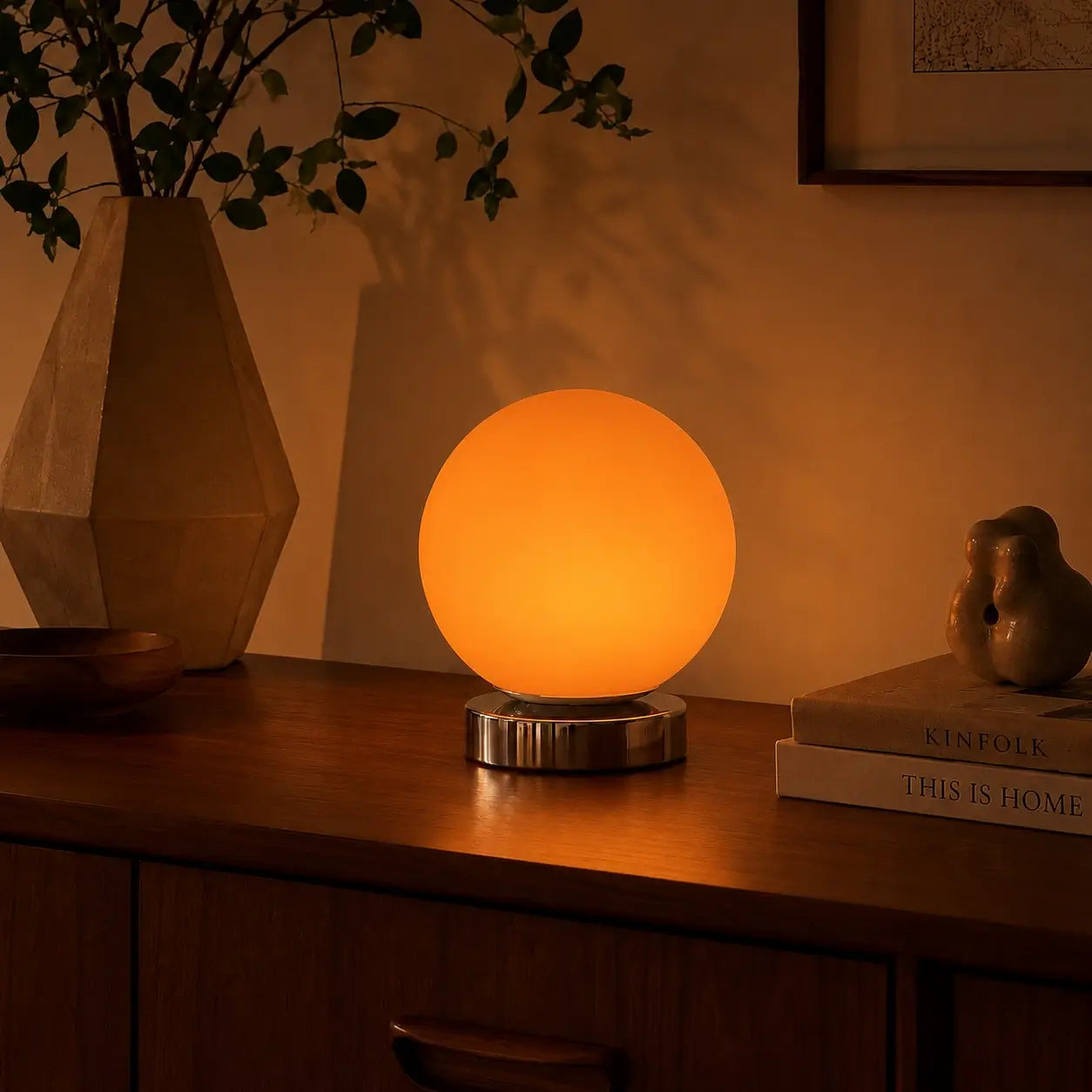 Lampe de bureau Ignis à globe orange allumée sur un buffet en noyer, lueur ambrée en soirée
