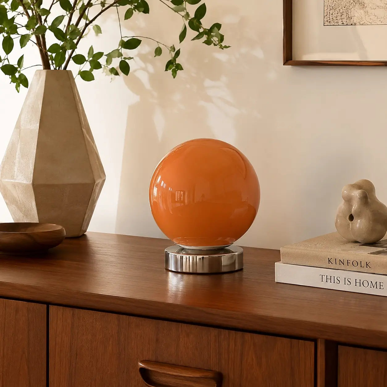 Lampe de bureau Ignis à globe orange posée sur un buffet en noyer parmi des objets céramique et un vase minéral