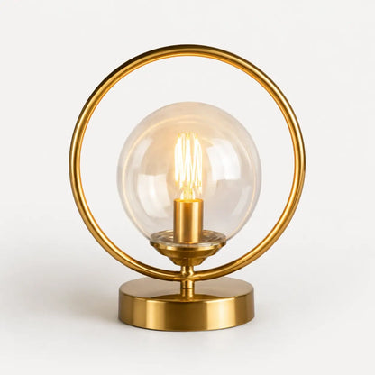Lampe de bureau en laiton doré à globe en verre transparent et anneau circulaire, modèle Orbis, allumée sur fond clair