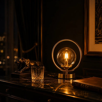 Lampe de bureau Orbis allumée le soir, filament Edison visible dans le globe en verre, lueur dorée sur marbre noir