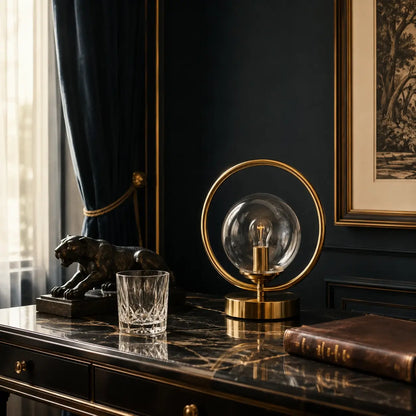 Lampe de bureau Orbis en laiton doré posée sur un bureau en marbre noir devant un mur bleu nuit, lumière naturelle