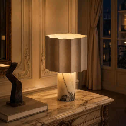 Lampe de bureau Sinus allumée sur une commode en marbre, lumière chaude et tamisée dans un salon parisien le soir