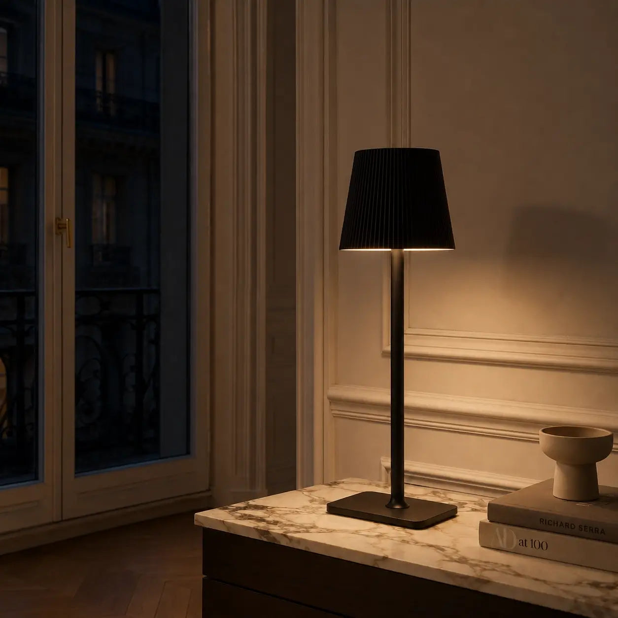 Lampe de bureau sans fil Lucerna noire allumée sur une console en marbre, lueur chaleureuse en soirée parisienne