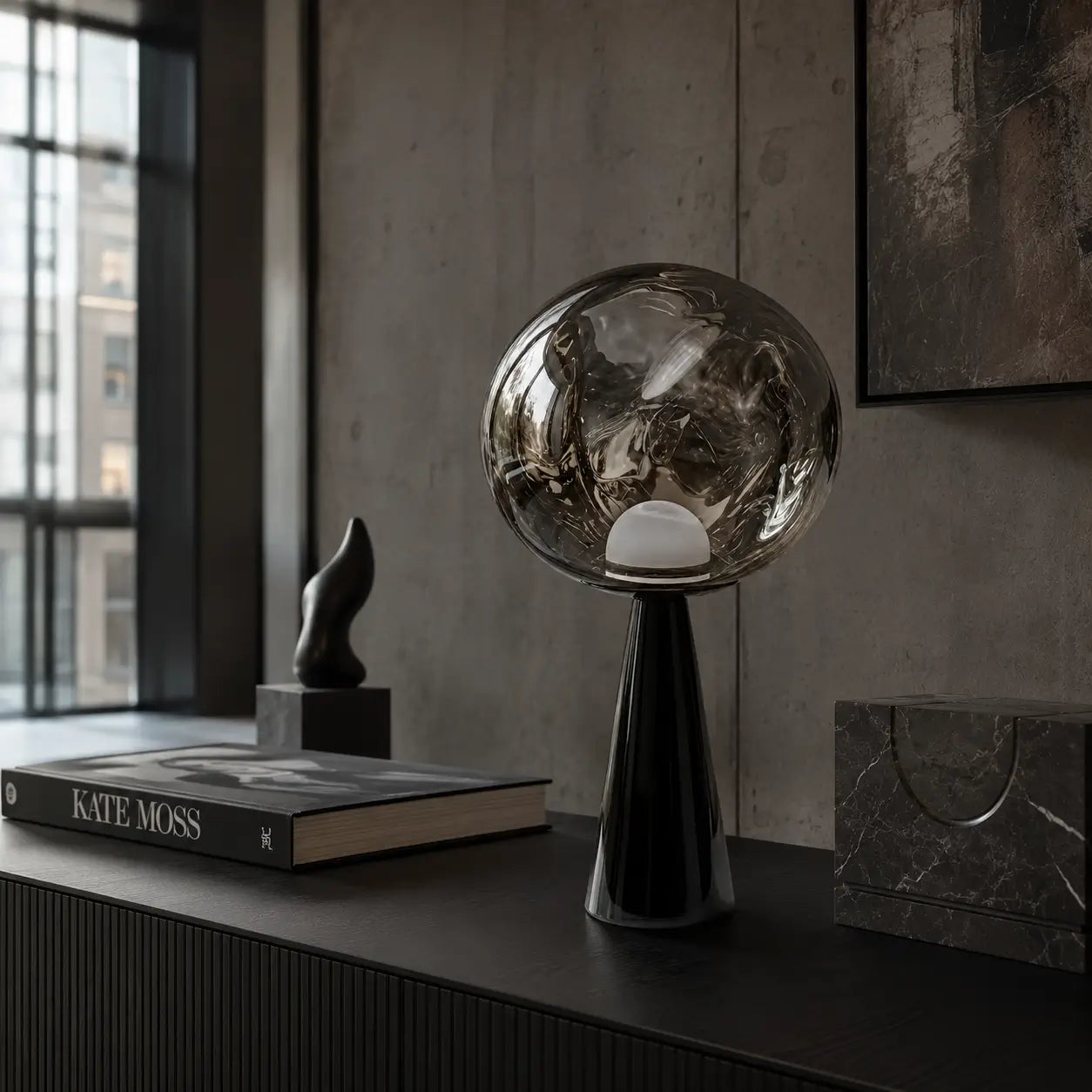 Lampe à poser Umbra en verre fumé posée sur un buffet noir dans un loft aux murs de béton