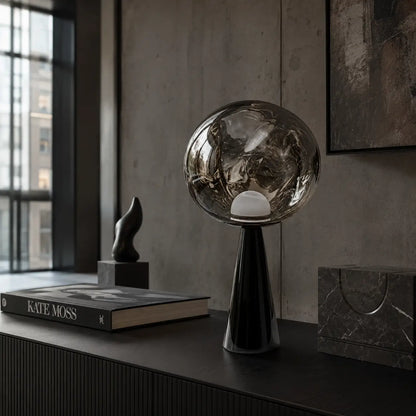 Lampe à poser Umbra en verre fumé posée sur un buffet noir dans un loft aux murs de béton